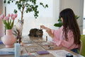 Bruna holding a pendulum over chakra boards while her two cats watch from the table