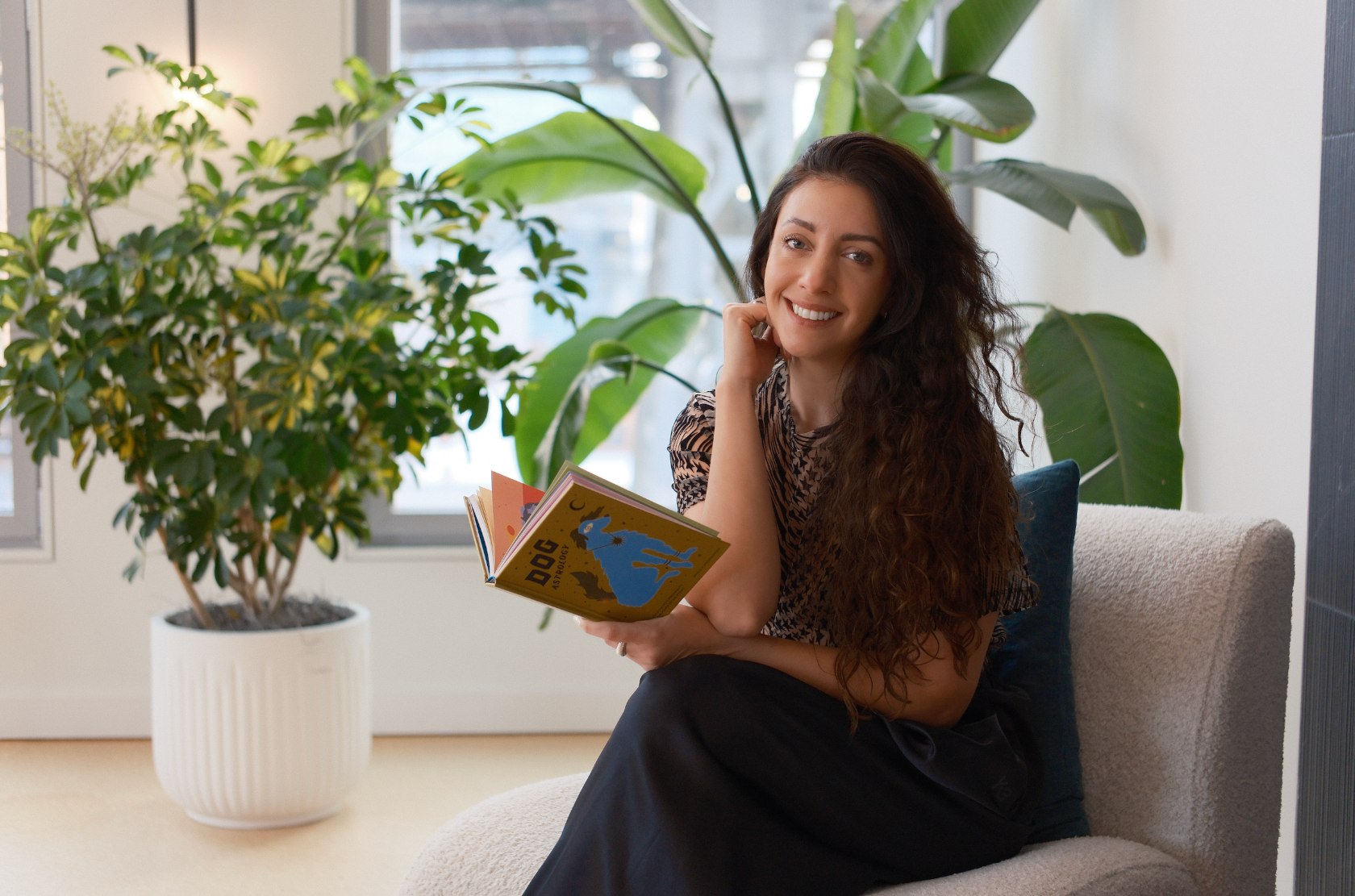 Bruna Fabregat smiling on her sofa, holding a book about dog astrology