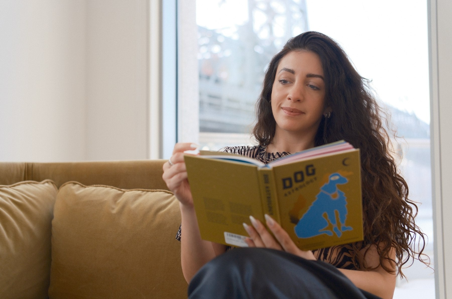 Bruna reading on her sofa by the window