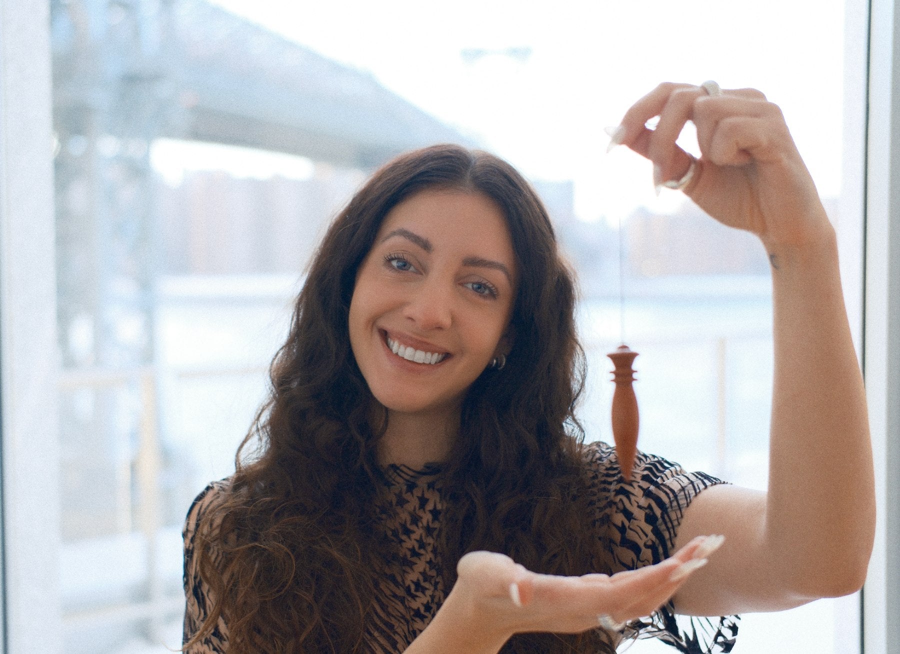 Bruna Fabregat smiling by the window, holding her pendulum